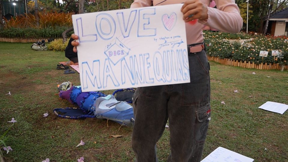 juno holds a sign up to the camera: love dice mannequins