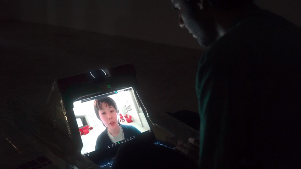the artist looks down at the console, which shows the face of miaki. They are having a video-call