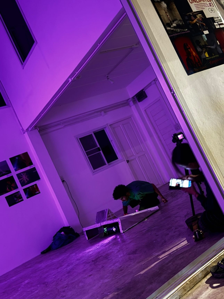 outside view of the artist leaning over the spaceship console. The room is tinted purple.