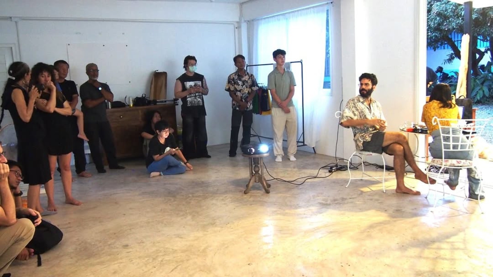 view of the artists seated at a small table inside the venue. stephan e perez turns to look at the audience, who are standing around the inside of the room